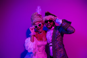 Fototapeta premium Two elegantly dressed individuals posing in vintage costumes under neon lights reflecting a lively party atmosphere