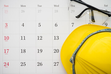 Flat lay of safety glass and yellow worker helmet on blank white calendar background copy space....