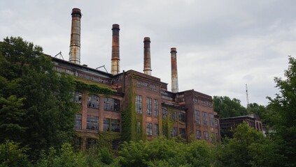 An old industrial building with tall smokestacks stands amidst dense foliage, showcasing the...