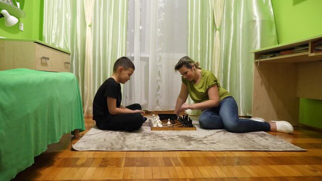 Mother and son playing chess at home. Leisure and board games.