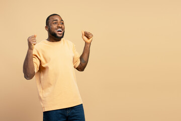 Excited young man celebrating victory with raised fists on beige background