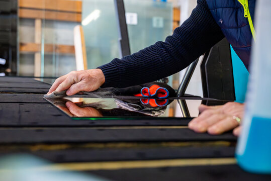 Dans un atelier de miroiterie, un technicien est en train de nettoyer le miroir.