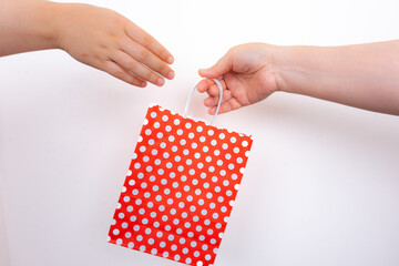 Two hands exchanging red polka dot gift bag on isolated white background. Hands holding red dotted shopping bag. Gift and celebration concept