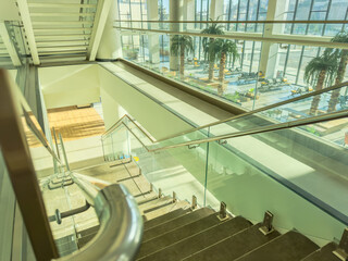 Modern glass staircases in bright indoor atrium with palm trees and sky view. Contemporary stairs...