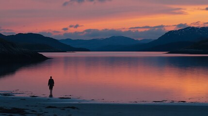 Solitary figure silhouetted against a vibrant sunset over a calm bay and mountain range.