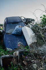 Abandoned car buried in trash evoking themes of environmental pollution and post-apocalyptic ruin