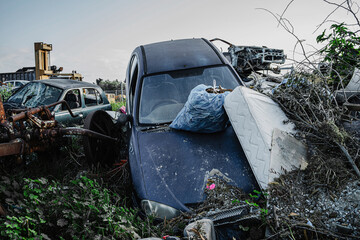 Abandoned car buried in trash evoking themes of environmental pollution and post-apocalyptic ruin