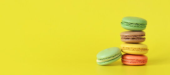 Stack of colorful macarons close-up. Bright French macarons on yellow background, side view. Assortment of macarons with different flavors. Delicious pastries, cookies, food background. Sweets tower