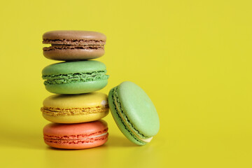 Stack of colorful macarons close-up. Bright French macarons on yellow background, side view. Assortment of macarons with different flavors. Delicious pastries, cookies, food background. Sweets tower