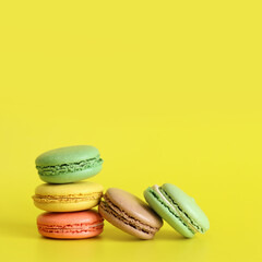 Several colorful macarons close-up. Bright French macarons on yellow background, side view. Assortment of macarons with different flavors. Delicious pastries, cookies, food background. Stack of sweets