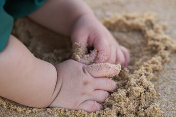 The baby is playing with sand, and the baby's foot is in the sand. The baby has a toothbrush in its mouth, which might be an unrelated object or part of the playtime activity.