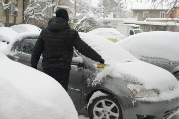 Man removing snow from a car in heavy winter conditions