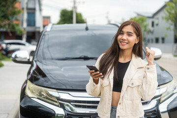 A young Asian woman drives a beautiful nature drive. she was standing in front of the car on the roadside. she uses the smartphone to call services.