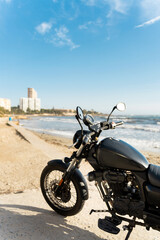 Fototapeta premium Black motorcycle parked on sandy beach with ocean view