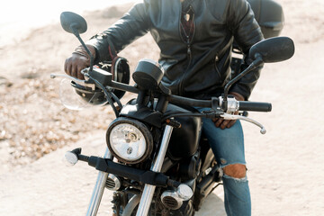 Biker wearing leather jacket and gloves is sitting on his motorbike