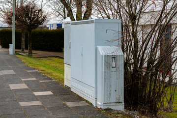 A pair of electric utility boxes is positioned beside a walkway in a quiet suburban neighborhood....