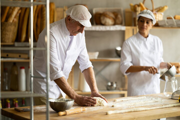 Elderly man and woman kneading and whipping dough