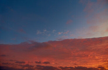 A fiery sky with clouds shimmering in sunset hues. Cirrus clouds reflect the last rays of the sun in the crimson evening sky. A scarlet sunset in the sky.