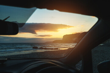 Sunset over the sea is seen through the windshield of a parked car