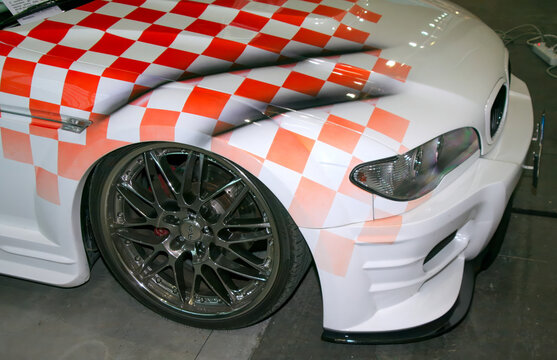 Rimini, Italy : 2019 03 29 Rimini Tuning free auto meeting A modified white BMW 3 Series with a checkered flag design on the hood and fender, showcasing its custom paint job.