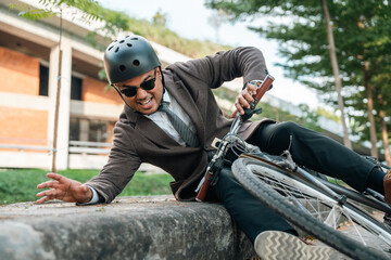 Asian Businessman falling off bicycle in city. Accident Injury leg pain. Broken leg Cyclist falls off the bike. Accident on the road.