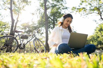 Young asian teenager learning with laptop sitting in the public park. Summer time spring young...