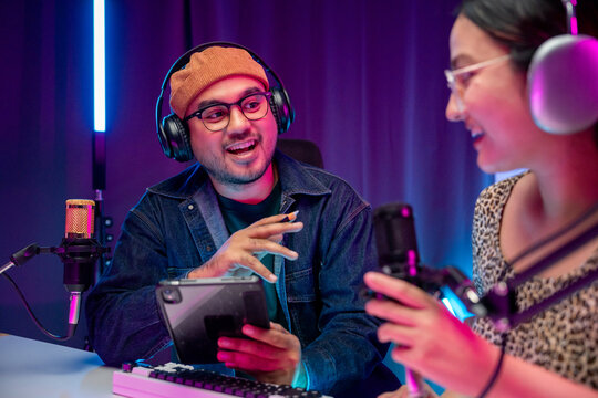 Young asian man and woman host streaming podcast with condenser microphone work on tablet at home broadcast studio. Content creator blogger recording voice over radio interview guest conversation