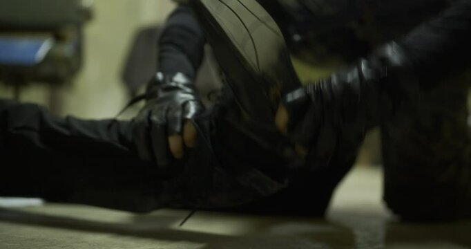 Spy in camouflage stealing unconscious man's shoes on cement floor - closeup