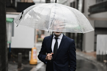 雨の中、傘をさす男性