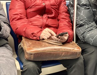 Unknown male passenger in a bright red jacket uses a smartphone while sitting comfortably on public...