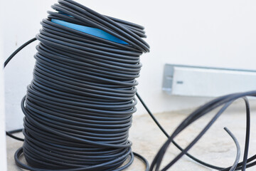large coil of black cable or wire, neatly wound and placed on the ground. The cable appears to be...