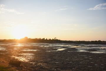 cracked and arid landscape under the setting or rising sun. The ground is extremely dry and split into numerous irregular patterns, indicating a severe lack of moisture.