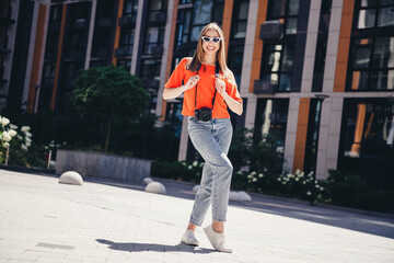 Young woman enjoying a sunny day in the city, stylish in casual clothing with a camera slung around...