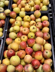 A mound of large red yellow coloured apples in boxes is displayed in the window of the supermarket's vegetable stand, demonstrating organic, vegetarian and healthy food. Close-up