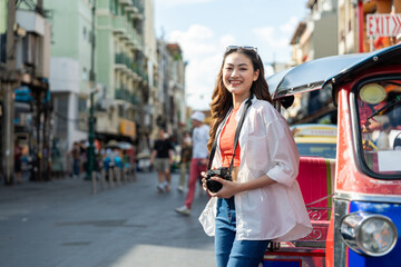 Fototapeta premium Young Asian woman traveling backpacker in Khaosan Road outdoor market in Bangkok Thailand. Happy female tourist walking in the downtown street traditional market