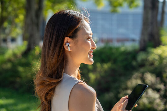 Young asian business woman with headset talking on smartphone standing in the garden public park. Cheerful woman discussion conference on smartphone - Powered by Adobe