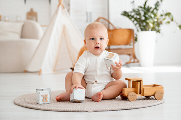 a kid plays with wooden toys, cubes and cars sitting on the floor in a bright children's room, a...