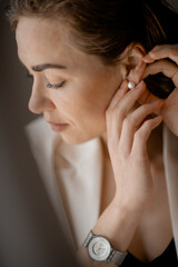 Obraz premium young woman putting on a pearl earring, focused on her reflection. The elegant, delicate accessory adds a touch of sophistication to her look, capturing a moment of beauty and grace