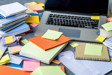 Cluttered workspace filled with notebooks, sticky notes, and laptop during a busy study session