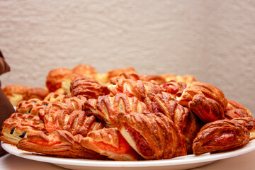 A variety of golden-brown pastries are piled high on a white plate, showcasing intricate patterns on their crusts. They appear freshly baked, with a flaky texture and some visible filling.