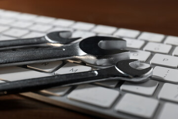 Technical support concept. Wrenches and keyboard on wooden background, closeup