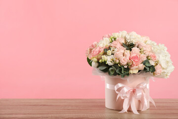 Beautiful bouquet in box on wooden table against pink background. Space for text