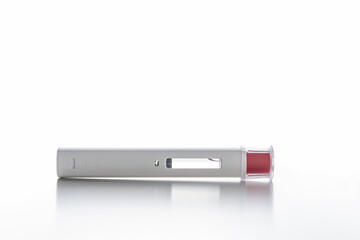 A white pen injector with a red tip for biological treatments such as Adalimumab, Etanercept or epinephrine. It is lying on a white light background, aseptic, clean, white and well lit.