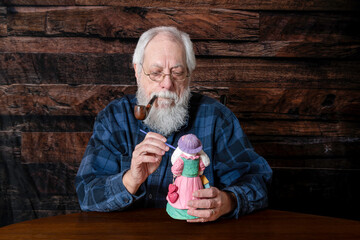 senior man with white beard smoking pipe painting Easter bunny with wood blank background