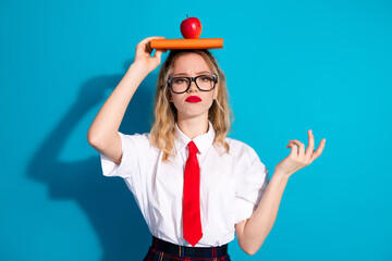 Young woman with glasses holding book and apple against blue background