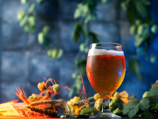 Cold refreshing light beer glass with drops. Green fresh hops and wheat ears on the table. Blue background