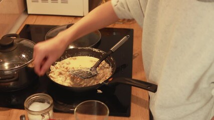 Young chef carefully preparing creamy chicken pasta dish while stirring ingredients in sizzling pan on modern stovetop, showcasing culinary skills and passion for home cooking