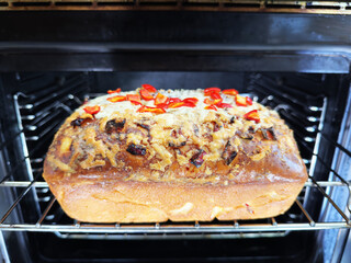 Closeup of a freshly baked loaf of homemade bread, with chopped jalapeno chillis and melted cheese, on an oven shelf.