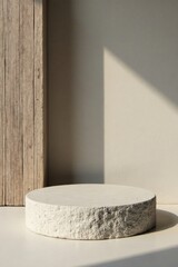 A sunlit minimalist display featuring a rough-textured circular platform beside a weathered wood plank against a neutral backdrop