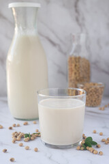 a glass of homemade soy milk with soy beans on white table background.